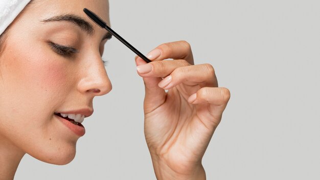 Sideways woman applying mascara on her lashes