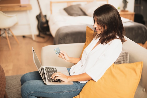 Free photo sideways woman holding a credit card and using her laptop