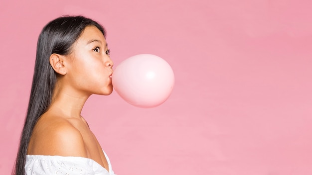 Free photo sideways woman inflates a pink balloon