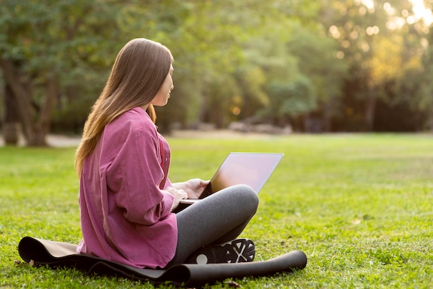 Боковая женщина смотрит на свой ноутбук в парке