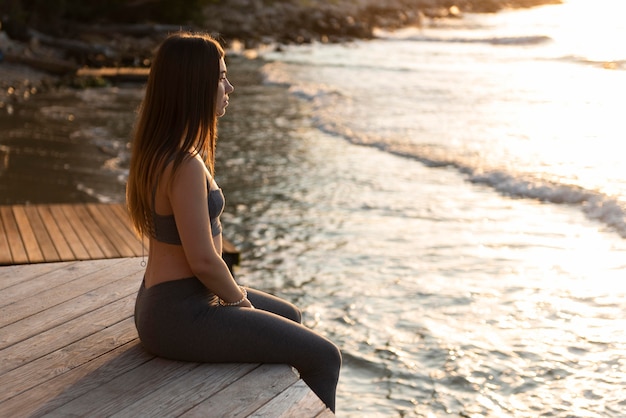 Sideways woman sitting next to the beach with copy space