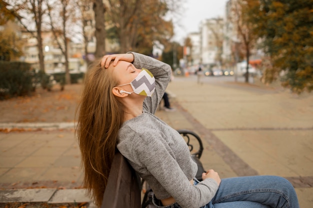Free photo sideways woman with medical mask sitting on a bench