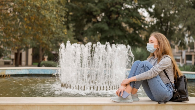 Sied view woman wearing a medical mask while sitting next to a fountain