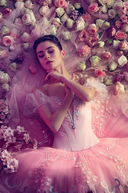 Молчание золото. Вид сверху красивой молодой женщины в розовой балетной пачке в окружении цветов. Весеннее настроение и нежность в коралловом свете. Концепция весны, цветения и пробуждения природы.