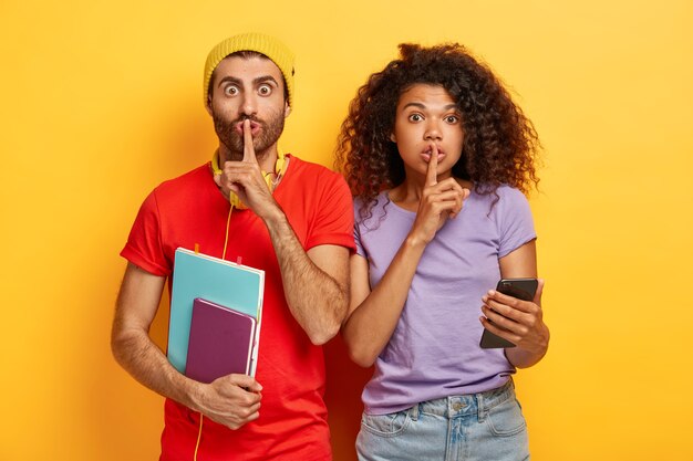 silent stylish couple posing against the yellow wall with gadgets