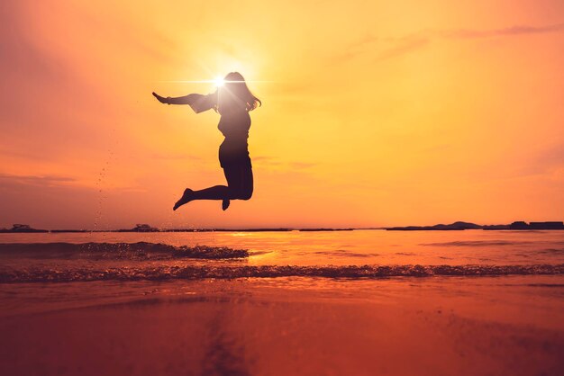 Silhouette of asian teen woman jump on sunset beach freedom ideas concept