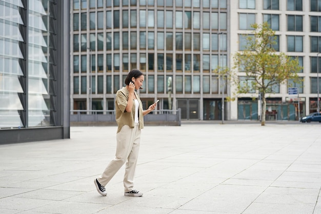 Silhouette of asian woman walking on street in wireless headphones holding smartphone