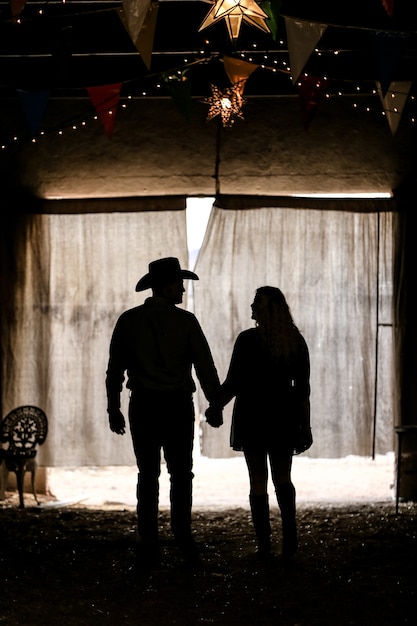 Silhouette of a couple holding hands in a tent under the lights