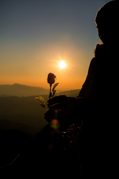 Silhouette of couple holding rose on hill at the sunset time skyline on background