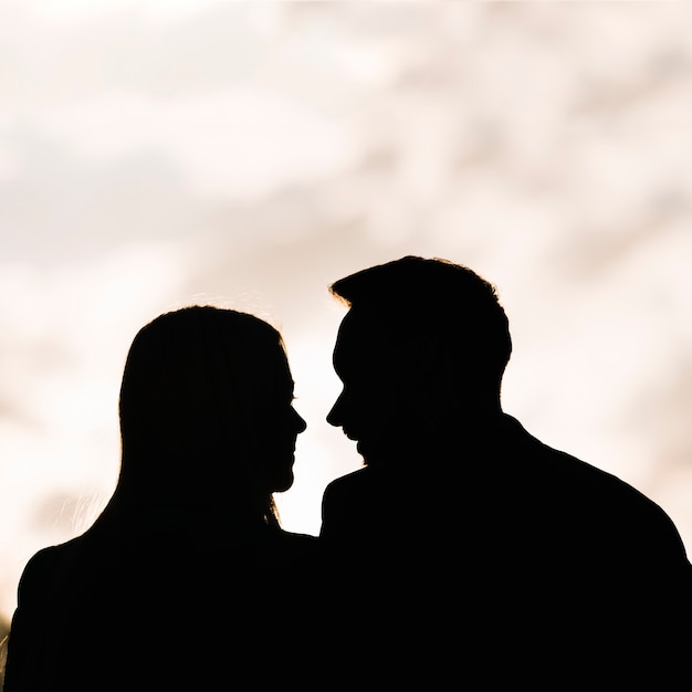 Silhouette of couple looking at each other against sky