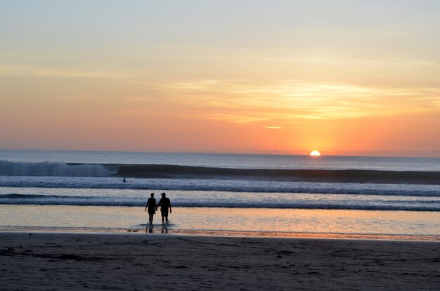 Silhouette of a couple walking in the water near the shore with a beautiful sky 