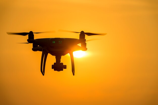 Silhouette drone with camera flying at sunset.