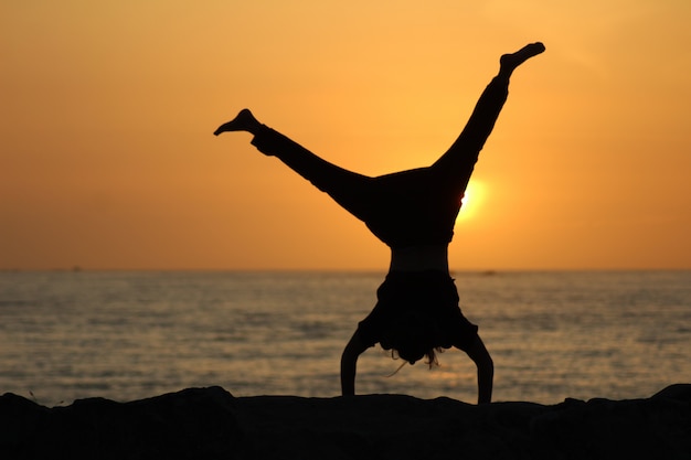 Silhouette of a female doing a cartwheel with a blurred sea and a clear sky