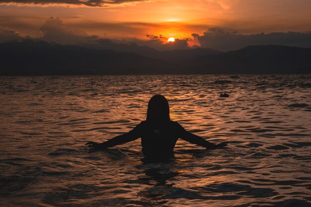 美しい日没時に海の水で半分の女性のシルエット
