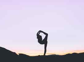 Free photo silhouette of a fit woman practicing yoga on a high cliff at sunset