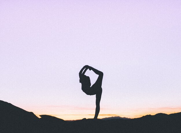 Silhouette of a fit woman practicing yoga on a high cliff at sunset