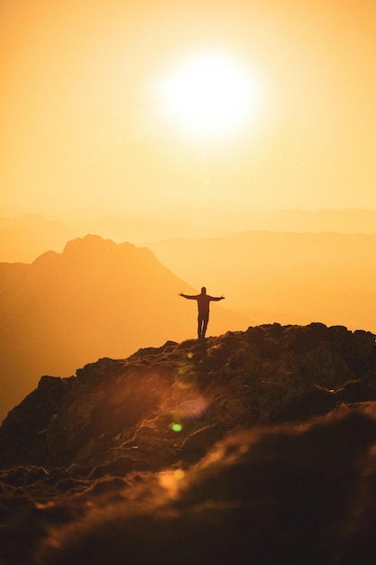 Силуэт беззаботного путешественника на вершине горы на золотом закате