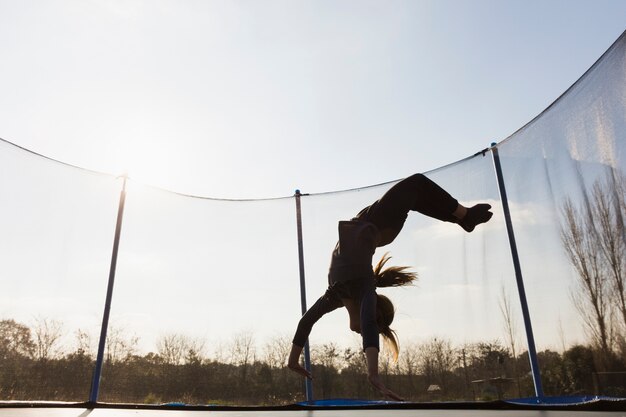 silhouette of girl jumping upside down on trampoline against the blue sky