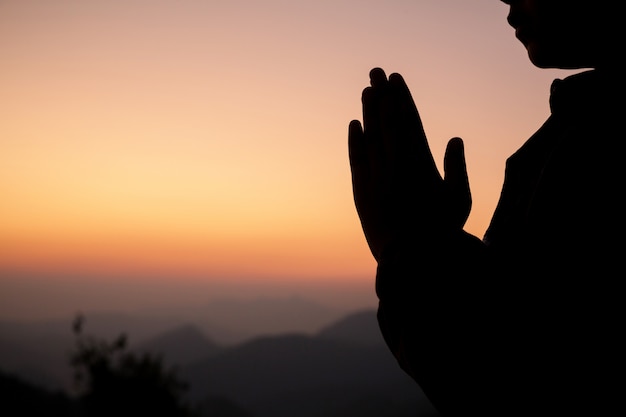 Silhouette of girl praying over beautiful sky background. 