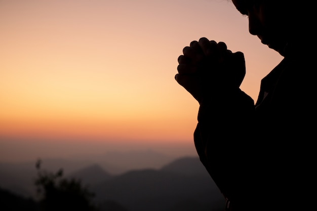 Silhouette of girl praying over beautiful sky background. 