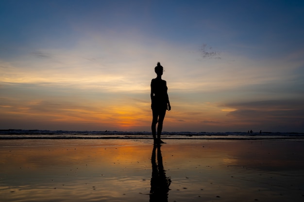 Силуэт девушки, стоя в воде на пляже, как солнце садится