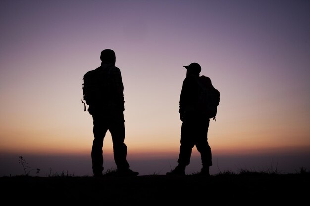 Silhouette of Hiker men with backpack stay on cliff and think on the top mountain at sunset Travel Lifestyle wanderlust adventure concept summer vacations outdoor