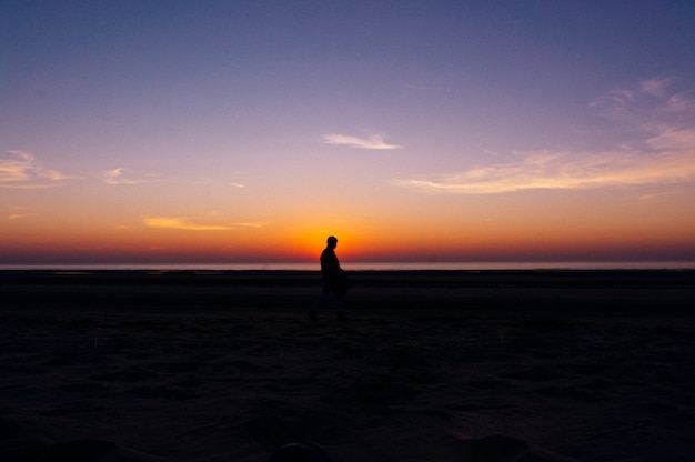 Silhouette of a lonely person walking on the beach with the beautiful view of sunset in background