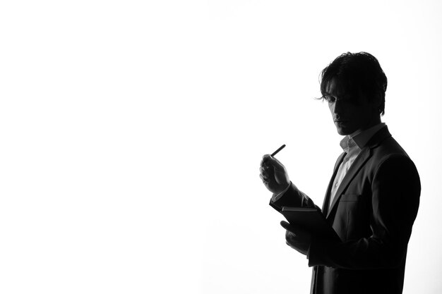 Silhouette of male in strict suit taking notes shadow back lit white background