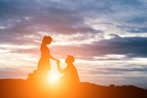 silhouette of man ask woman to marry on  mountain background.