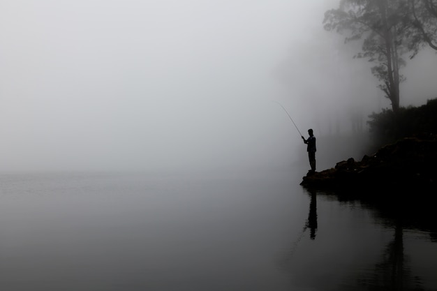 Силуэт человека, ловящего рыбу на озере с густым туманом на заднем плане