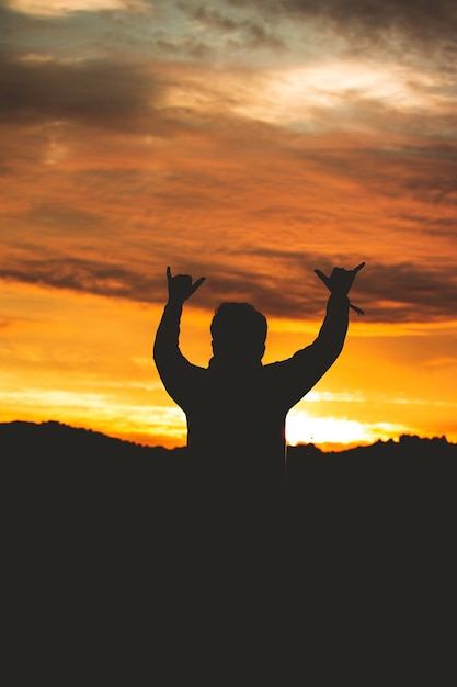 Silhouette di un uomo che fa un segno con le dita sul colorato cielo al tramonto