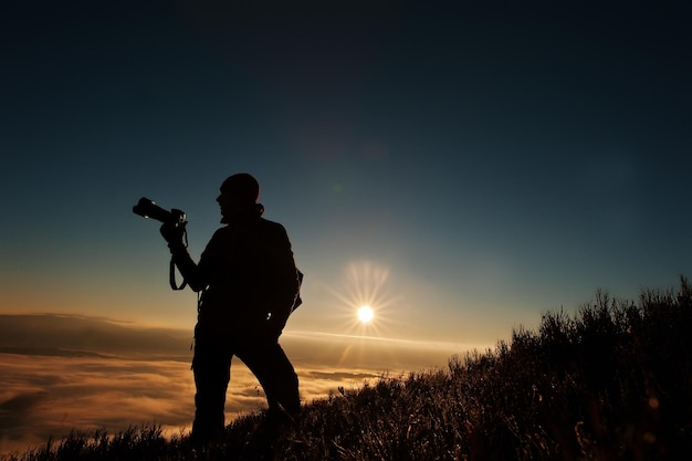 Silhouette of man photographer with camera on hand background mountains on sunset with fog Amazing shot of beauty world and human