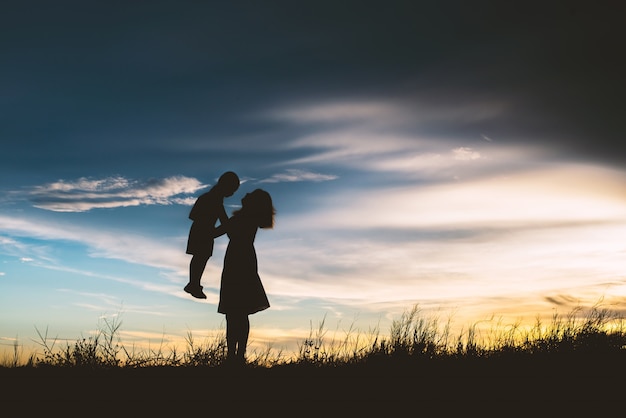 Silhouette of mother playing with her son in the meadow