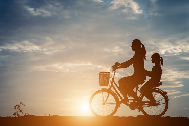 Silhouette of mother with her daughter and bicycle