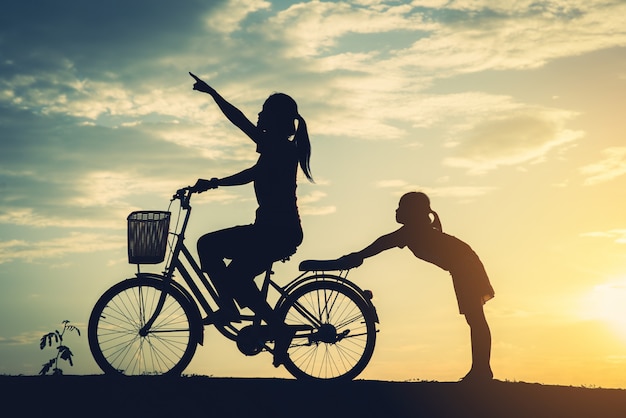 Silhouette of mother with her daughter and bicycle