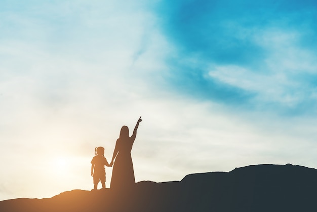 Siluetta della madre con sua figlia in piedi e tramonto