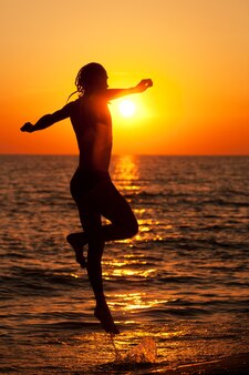 여름날 화려한 황금빛 일몰 동안 바닷물 가장자리에서 달리는 젊은 운동 남자의 실루엣. 휴가, 여행, 활동적인 건강한 라이프 스타일 개념