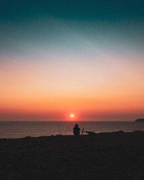 일몰 동안 해안에 앉아있는 사람의 실루엣