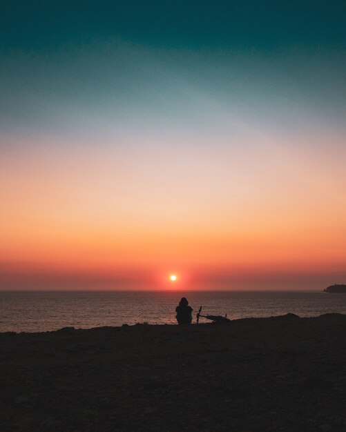 Silhouette of a person sitting on the shore during sunset
