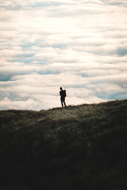 Silhouette of a person standing on a grassy hill with a cloudy sky