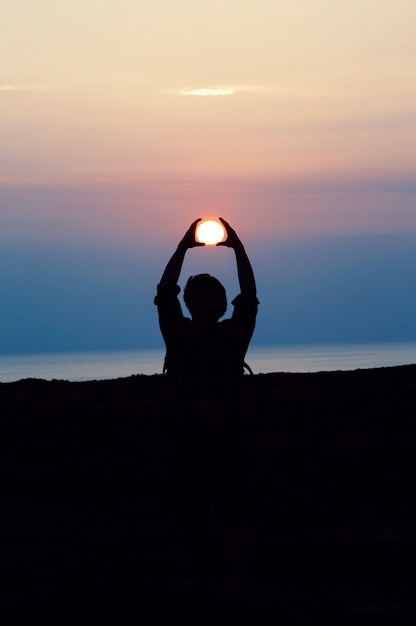 Silhouette of person with both hands over his head tracing the sun during golden hour