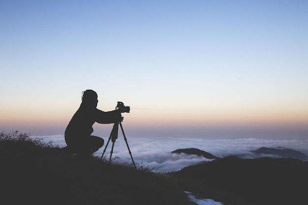 Силуэт фотографа, настраивающего камеру для съемки моря облаков во время заката