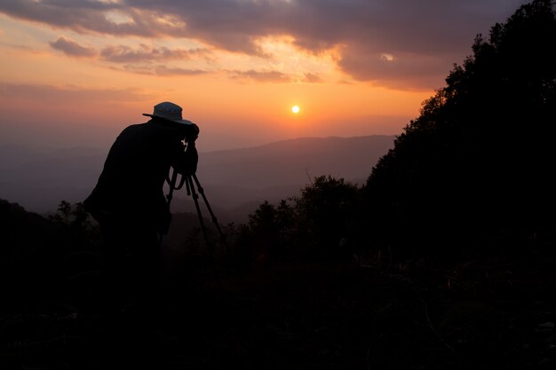 山の夕日を撮影する写真家のシルエット