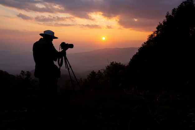 山の夕日を撮影する写真家のシルエット