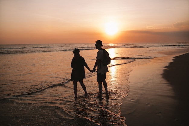 Silhouette portrait of young romantic couple walking on the beach. Girl and her boyfriend posing at golden colorful sunset