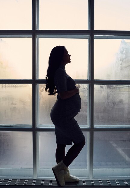 Silhouette of pregnant woman near big window.