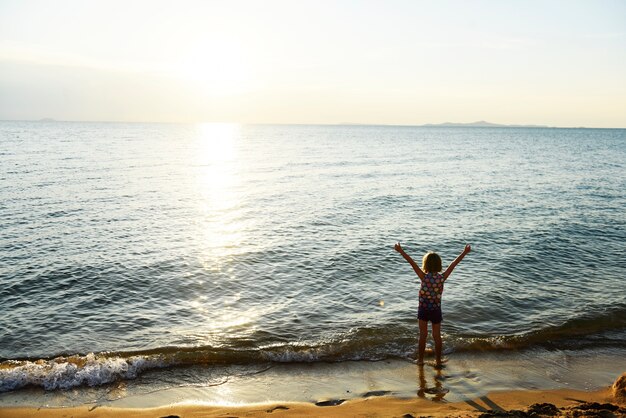 Silhouette rear view of young caucasian girl with arms raised at the beach alone