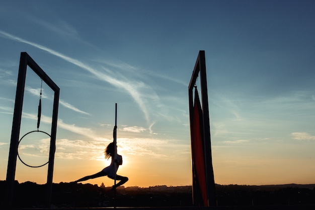 Siluetta del ballerino del palo sexy che esegue sul tetto al tramonto