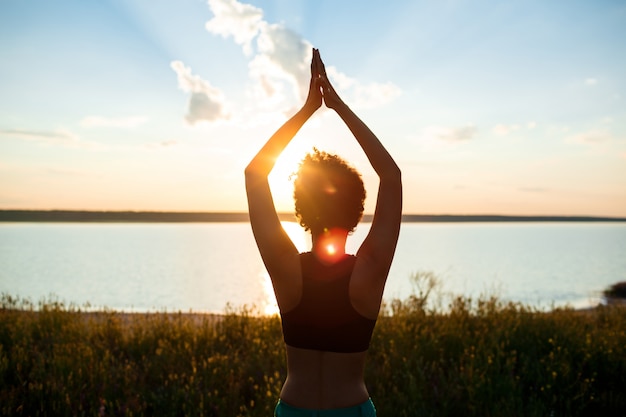 Silhouette of sportive girl practicing yoga in field at sunrise.