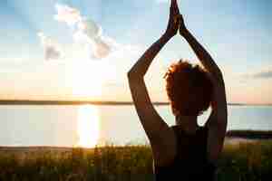 Foto gratuita siluetta di yoga di pratica della ragazza allegra nel campo ad alba.